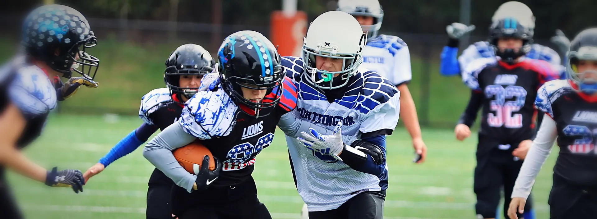 A Lions ball carrier powers through a Worthington defender, ball tucked, the pursuit closing behind him.
