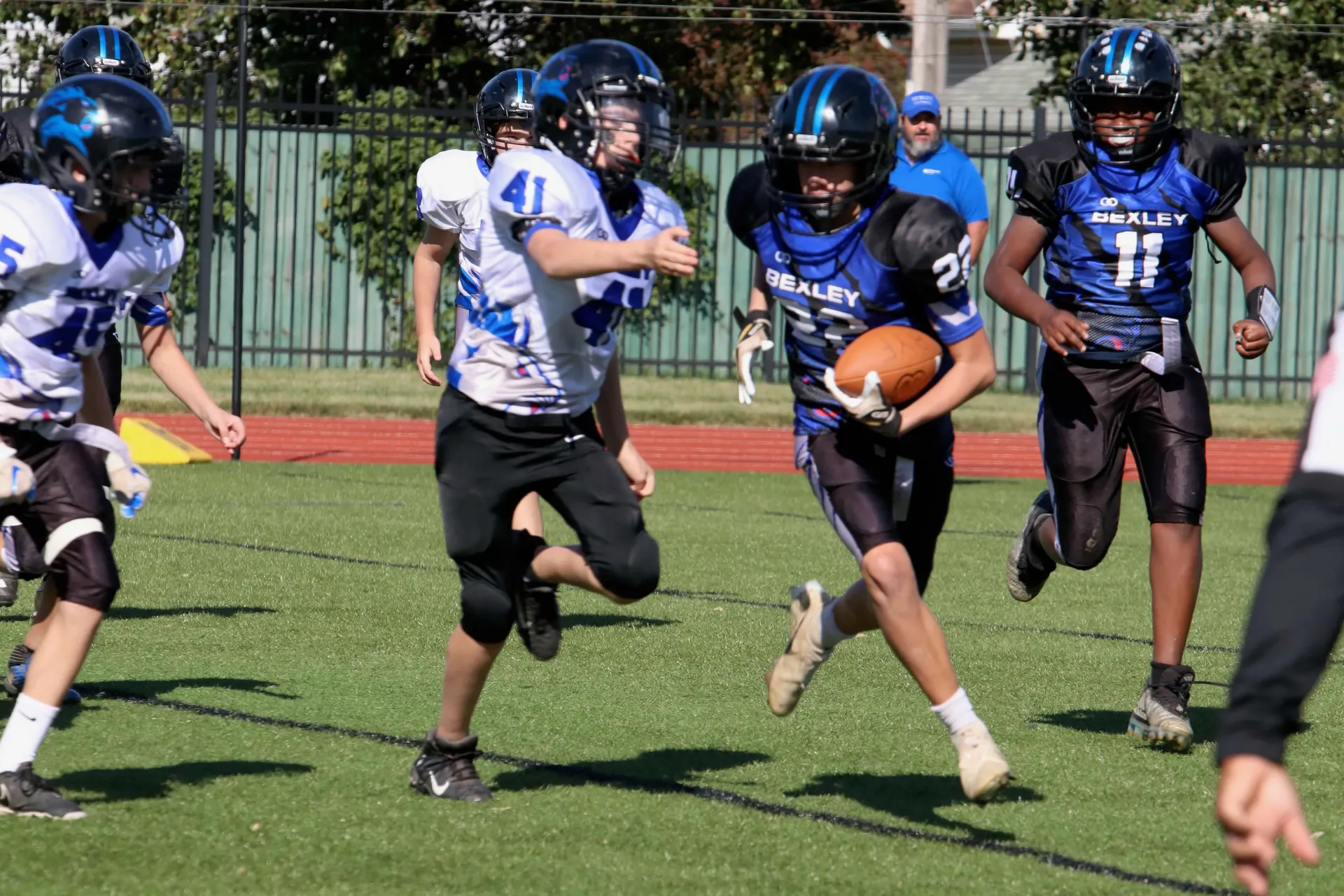 A Bexley ball carrier turns the corner in the sun, a teammate trailing and the chase closing behind him.